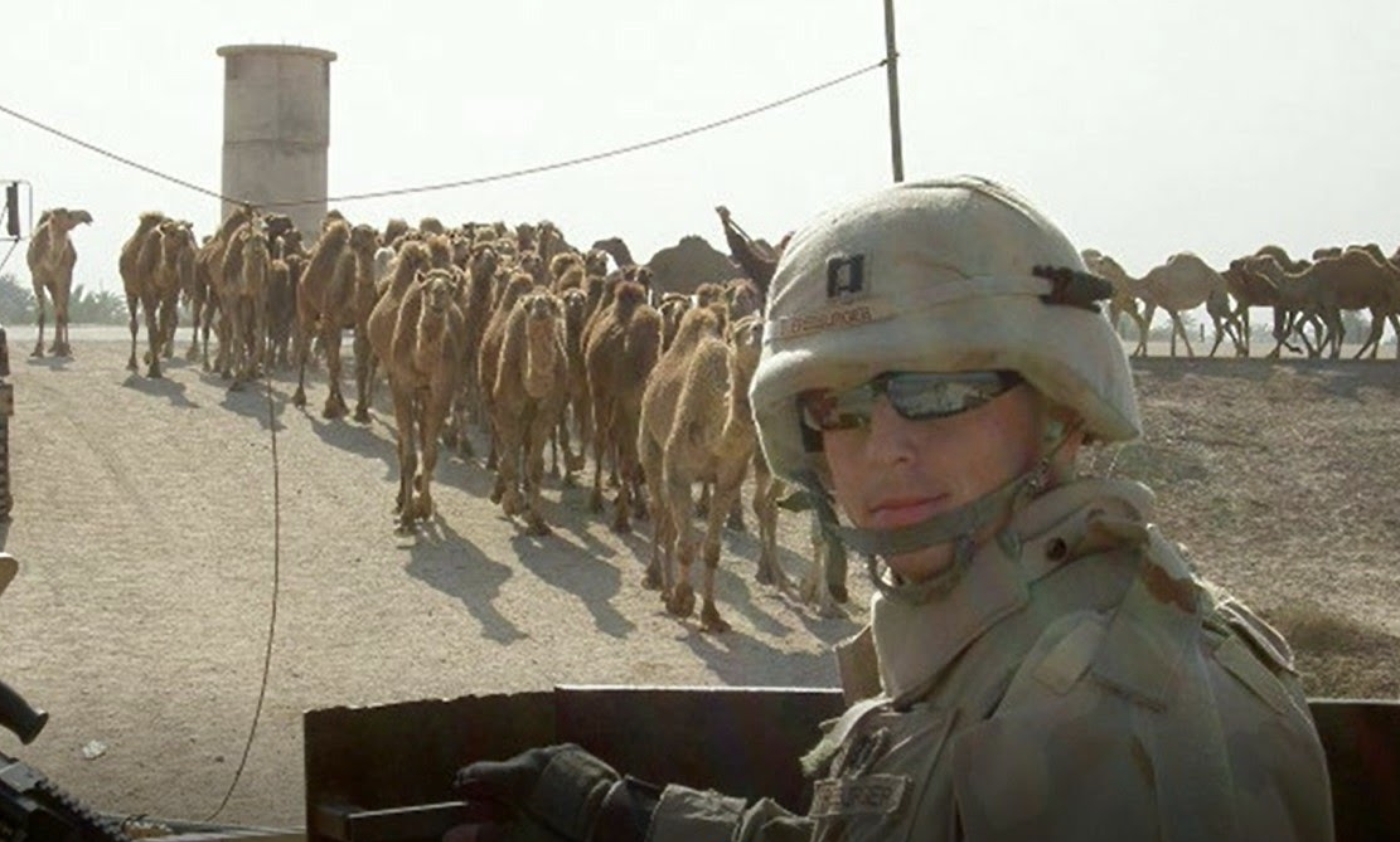 Patrick Freeburger during a military deployment overseas, with a line of camels in the background